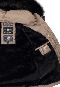 Navahoo-Mantelinnenseite mit weichem schwarzen Kunstfell-Futter, beigem synthetischen Außenmaterial, auffälligen Logo-Tags und einer Taschenklappe mit Druckknopfverschluss.