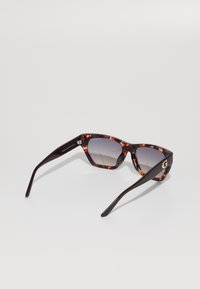 Tortoiseshell zonnebril met geometrische montuur, gradient lenzen en donkerbruine armen, met een gouden accent op de poot.