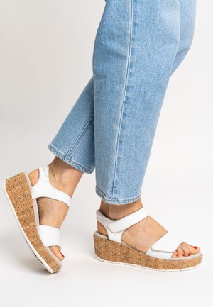 Weiße Keilsandalen mit Korksohle, ausgestattet mit breiten Riemen und einem abgerundeten Zehendesign. Die Absatzhöhe beträgt etwa 6 cm.