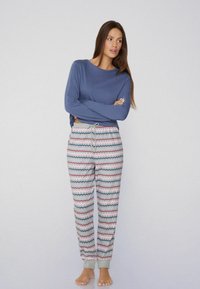 Camiseta azul de manga larga y corte acogedor, combinada con pantalones de chándal de patrones en zigzag multicolores que cuentan con una cintura ajustable y puños grises en los tobillos.