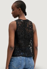 Top in pizzo nero con motivo floreale, design senza maniche e chiusura posteriore. Abbinato a jeans in denim, che mettono in evidenza il tessuto testurizzato e dettagli intricati.