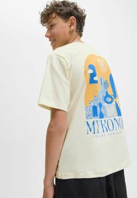 Camiseta amarilla de manga corta con un diseño gráfico azul que presenta formas abstractas y el texto "MYKONOS PURE PARADISE" en la parte posterior.