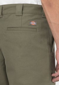 Pantaloni Dickies verde oliva, con una tasca sul retro e una patch con il marchio. Il tessuto presenta un aspetto testurizzato e resistente.
