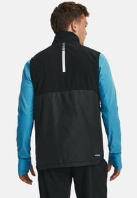 Gilet sans manches noir avec un col haut, présentant une bande réfléchissante blanche dans le dos, et des manches longues bleues en dessous.