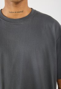 Mørkegrå bomulds t-shirt med rund hals og korte ærmer, der har en glat tekstur og diskrete syningsdetaljer.