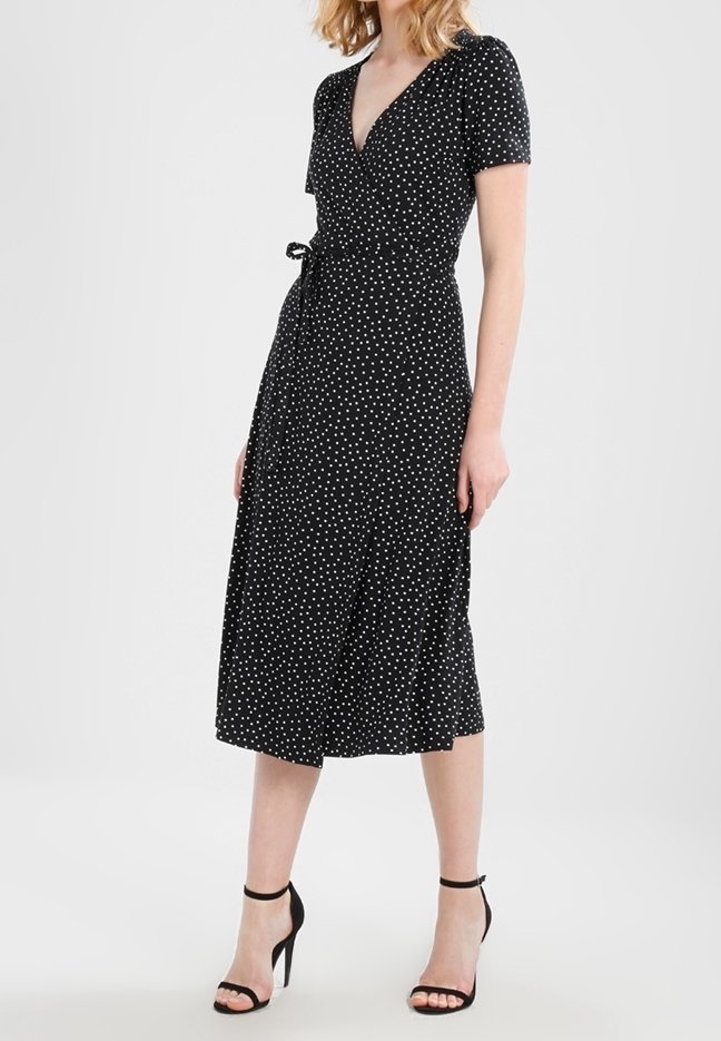 Czarna sukienka typu wrap z białymi kropkami, krótkimi bufkami, dekoltem w serek i związanym w pasie. Długość do połowy łydki z zwiewną spódnicą.