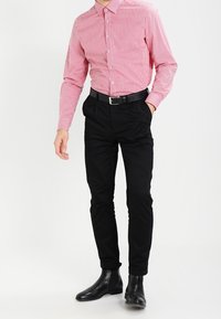 Camicia a righe rosse e bianche, pantaloni neri con finitura testurizzata, cintura nera e stivaletti neri. Design semplice, vestibilità su misura.