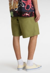 Olivenfarvede shorts med en afslappet pasform, lavet af bomuld, med to baglommer. Båret med gule sneakers og hvide ankelsokker.
