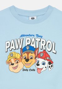 Felpa azzurra chiaro con tre personaggi di cani cartoni animati che indossano cappelli. Il testo include "Adventure Bay," "PAW PATROL," e "Duty Calls."