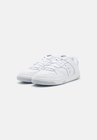 White sneakers with a smooth leather upper, rounded toe, lace-up design, perforated detailing, and contrasting blue accents on the tongue.