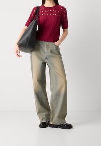 Punainen neulepaita, jossa on leikattu kuvio ja ribbikudos, yhdistettynä vaaleansinihin, leveälahkeisiin farkkuihin. Musta nahkabag ja mustat kengät.