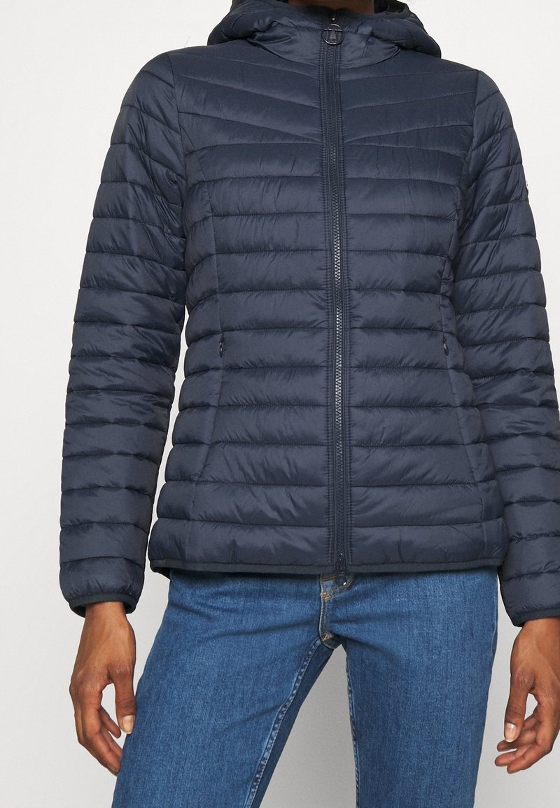 Veste matelassée bleu marine avec une coupe ajustée, un matelassage horizontal, deux poches latérales et une capuche. Fermeture éclair et matériau léger.