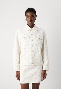 Veste en denim blanc avec un motif floral rose, boutons-pression, deux poches poitrine et un col. Assortie à une jupe correspondante.