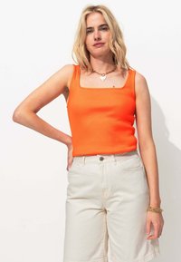 Débardeur côtelé orange vif avec un décolleté carré, associé à un short taille haute beige clair. Détail de collier en chaîne métallique simple.
