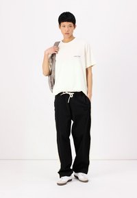 Cremefarvet T-shirt med korte ærmer og blåt logo, parret med sorte træksnorbukser med hvide sidelister, og hvide sneakers.