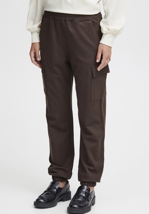 Bruine cargobroek met een elastische tailleband, zijzakken en geribbelde manchetten, gecombineerd met zwarte loafers met een decoratieve band.