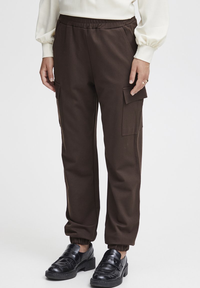 Bruine cargobroek met een elastische tailleband, zijzakken en geribbelde manchetten, gecombineerd met zwarte loafers met een decoratieve band.