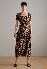 Svart blommig midiklänning med puffärmar, prydd med rosa och gula blommor, matchad med en svart kuvertväska och svarta sandaler i slide-modell.