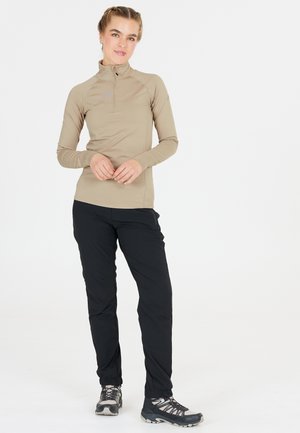 Beige long-sleeve top with a half-zip collar, paired with black tapered pants and gray hiking boots with textured soles.