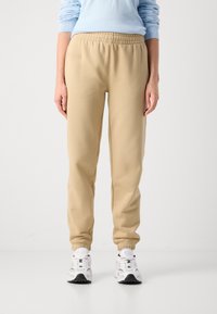 Beige sweatpants med elastisk midja, avslutade anklar och en mjuk textur. Matchas med vita sneakers med svarta accenter.