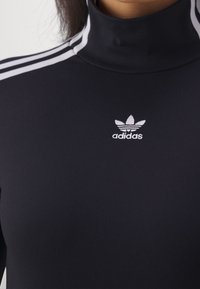 Czarny golf z trzema białymi paskami na ramionach. Posiada małe białe haftowane logo Adidas na klatce piersiowej.