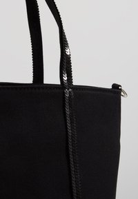 Borsa tote nera in tela con tessuto testurizzato, tracolla in sequins neri lisci e un design semplice con dettagli in metallo.