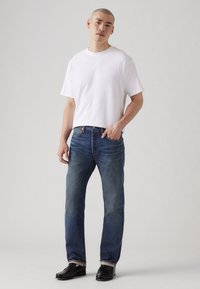 Camiseta blanca de algodón combinada con jeans de mezclilla azul. Los jeans son de corte recto con desgastado, y el conjunto se completa con zapatos de cuero negros.