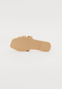 Tan rubberikengä sole, jossa on tekstuuripinta, sileät alueet ja pyöreät korostukset. Tasainen muotoilu tarjoaa vakautta ja mukavuutta.