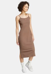 Abito midi marrone a coste con spalline sottili e spacchi laterali, dotato di un piccolo logo del marchio sul petto. Abbinare a sneakers bianche e calze.