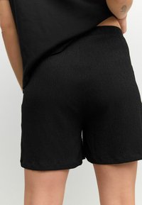 Pantaloni corti neri realizzati in tessuto testurizzato, dotati di una vita elastica e di una vestibilità comoda. L'orlo è leggermente arrotolato per un tocco di dettaglio.