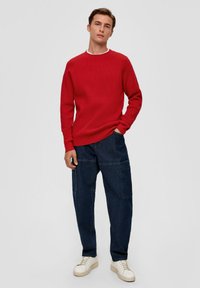 Rode ribbeltrui met een ronde hals, gecombineerd met donkerblauwe cargo broek en lichtgekleurde sneakers, wat zorgt voor een casual outfit.