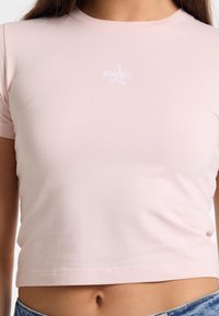 Pink cropped T-shirt made of soft cotton. Features short sleeves and a small embroidered star logo in white on the chest.