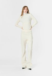Jumpsuit de crema claro con mangas largas y cuello alto, combinado con pantalones acampanados a juego. Tejido suave con un diseño ajustado y sutiles acentos de costura.