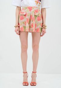 Pantaloni corti a stampa floreale con motivi di foglie rosa e verdi, dotati di due tasche frontali, realizzati in tessuto leggero; abbinati a sandali con tacco arancioni.