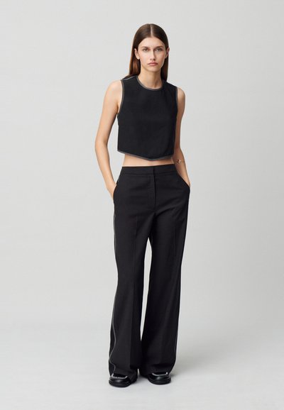 Top negro sin mangas y corto con un dobladillo curvado y costuras en contraste, combinado con pantalones anchos negros. Ambas prendas tienen una textura suave.