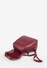 Bordeauxfarbene Leder-Rucksack mit quadratischer Form. Verfügt über eine Reißverschlussöffnung, glatte Oberfläche und ein dezentes Logo auf der Vorderseite. Innen ist er mit Stoff ausgekleidet.