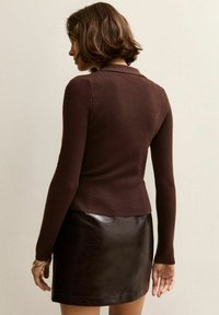 Brązowy sweter z prążkowanego dzianiny z kołnierzykiem, dopasowany fason i długie rękawy, zestawiony z krótką czarną skórzaną spódnicą.
