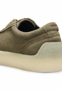 Baskets en daim vert olive à la forme arrondie, dotées d'une semelle en caoutchouc claire et légèrement translucide, avec des détails cousus sur la tige.