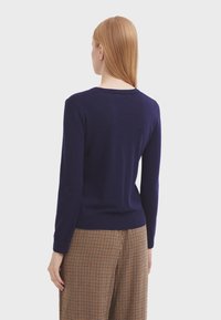 Maglione a maglia blu navy con maniche lunghe e collo rotondo, caratterizzato da una texture liscia e orlo a coste, indossato con pantaloni a quadri.