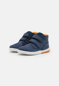 Adidași navy blue până la gleznă, din suede, având o talpă din cauciuc alb, două curele cu arici și o căptușeală interioară portocalie.