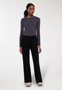 Maglia grigia a maniche lunghe abbinata a pantaloni neri a gamba larga. Tessuto testurizzato, vita elasticizzata. Sneakers bianche con suola marrone chiaro.