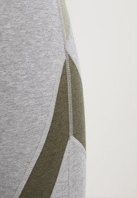 Tessuto elasticizzato grigio e verde oliva con design a pannello diagonale. Texture morbida, cuciture a punto e accenti a blocchi di colore.