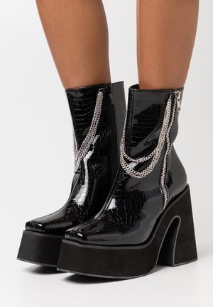 Czarne lakierowane botki za kostkę z teksturą krokodylej skóry, srebrne akcenty w postaci łańcucha, podwójne zamki błyskawiczne oraz grube czarne platformy.