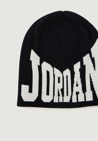 Crna pletena kapa s velikim bijelim natpisom "JORDAN". Mekana tekstura, zaobljeni vrh i čvrsto pristajanje. Naglašena hrabrim tipografskim rješenjem.