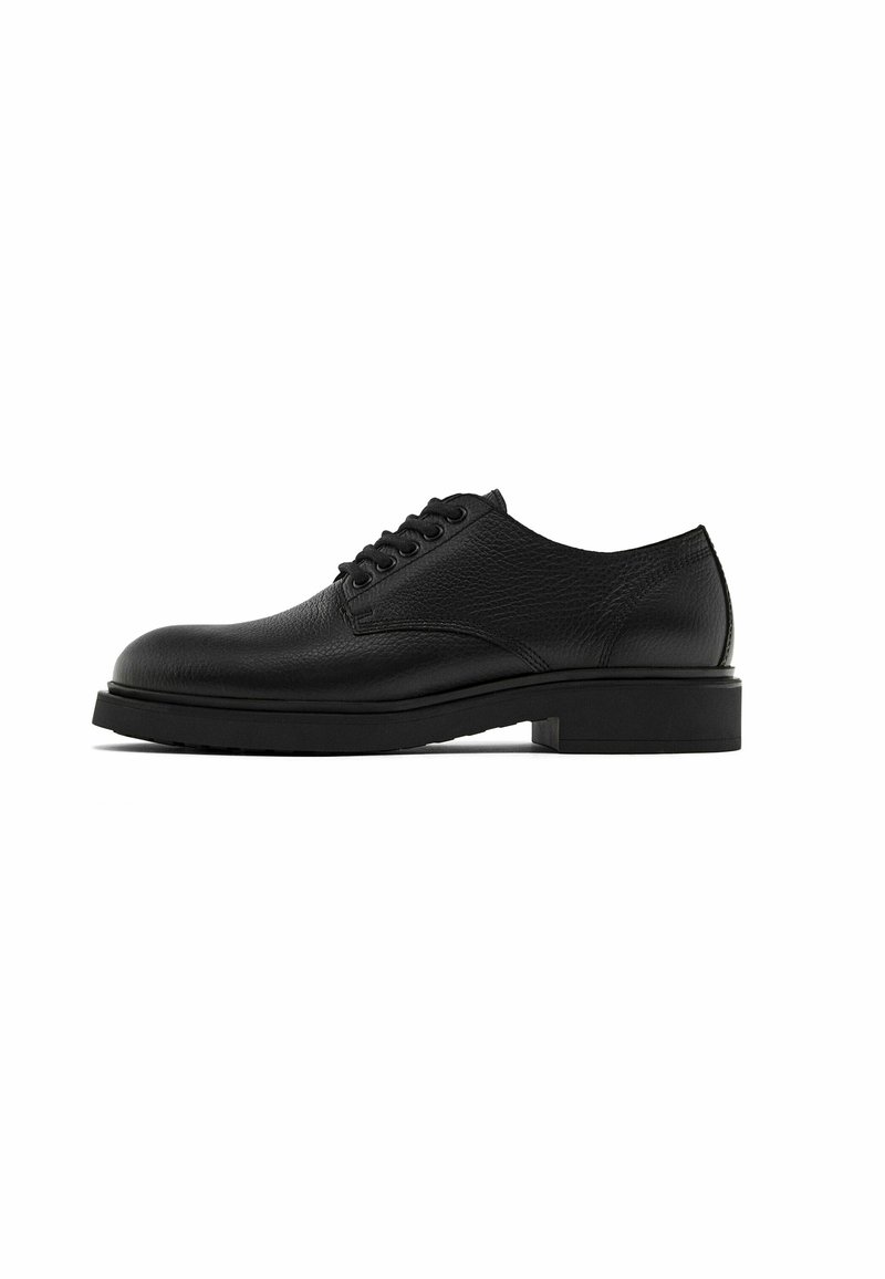 Chaussure Oxford en cuir noir avec bout arrondi, six œillets avec lacets noirs, empeigne en cuir texturé et semelle épaisse plate.
