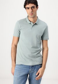 Lys grønn polo-skjorte med krage og korte ermer, har en subtil brodert logo på brystet, laget av bomull.