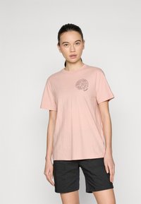 Rosa bomull t-skjorte med korte ermer, med et sirkulært grafisk trykk på brystet. Kombinert med svarte cargo-shorts. Enkelt design.