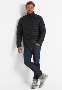 Black, puffer jacket with horizontal quilted pattern, high collar, front zipper, and left chest pocket. Worn with dark jeans and gray sneakers.