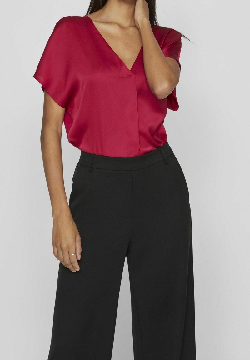 Blouse en satin rouge avec un col en V et des manches courtes, associée à un pantalon noir à jambes larges, présentant une texture lisse et un design simple.