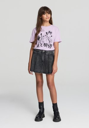 T-shirt grafico lilla con illustrazioni nere, abbinato a una gonna di jeans nera a vita alta e stivali neri con tacco chunky.
